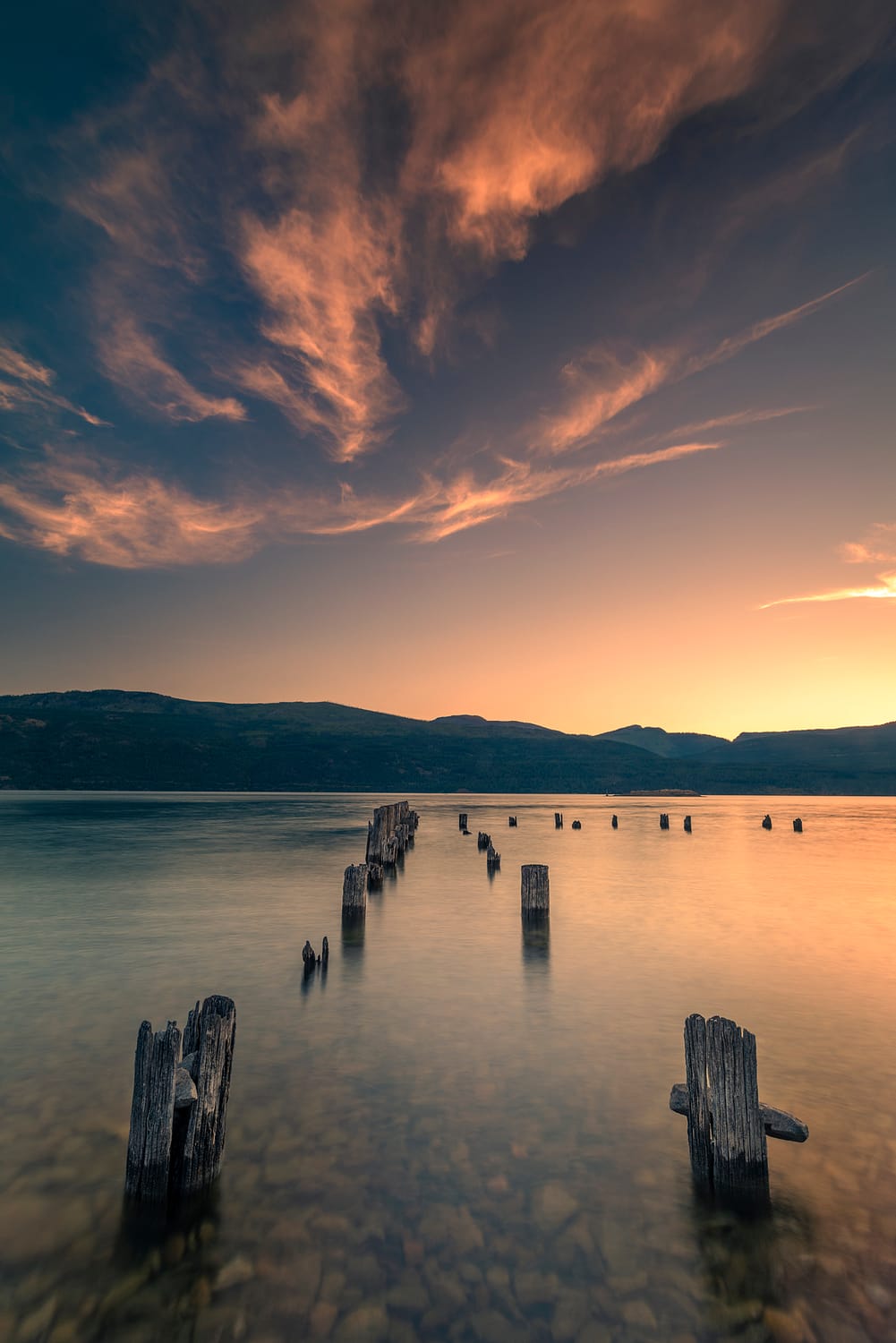a sunrise over a body of water with rocks and abandoned dock in the foreground