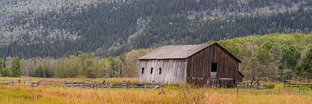 an old barn in a field with a mountain in the background