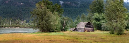 an old barn in a grassy field along a river