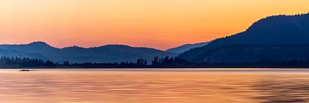 a sunset over a body of water with a mountain in the background