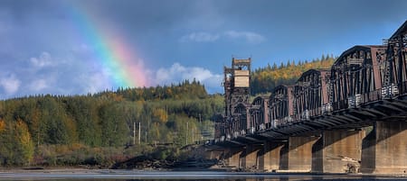 a train bridge over a body of water with a rainbow in the background