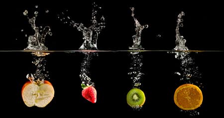 aline of fruit dropped in water creating a splash