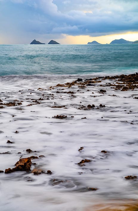 a rocky beach next to the ocean with islands in the background in Hawaii