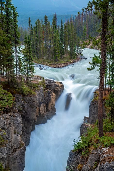 a large waterfall in a forest with Sunwapta Falls in the background