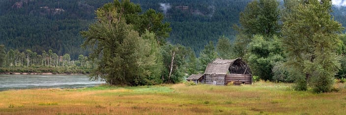 an old barn in a grassy field along a river