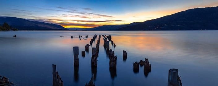 a sunrise over a body of water with an abandoned dock
