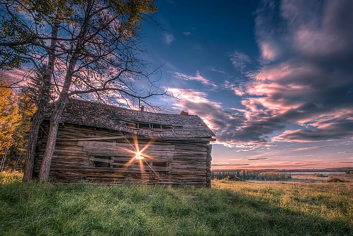 a sunrise over a grass field with an old barn