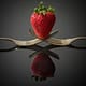 a strawberry held by two forks with a reflection